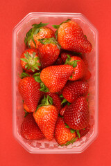 A clear plastic container holds a cluster of vibrant red strawberries with green caps, positioned...
