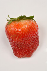 A single, ripe red strawberry with green leaves is isolated on a plain light background