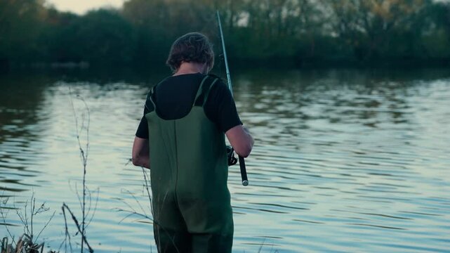 Carp fisherman wearing waders in a lake with fishing rod
