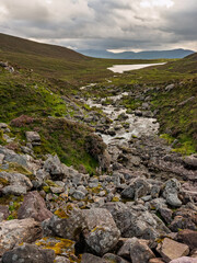 The Cottoners River flows gently through a rocky terrain in the heart of Ireland, surrounded by lush greenery and distant mountains under a moody sky.
