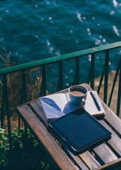 Tablet on a sunlit balcony table with sea view. Morning on the French Riviera, elegant slow lifestyle, film photo style.