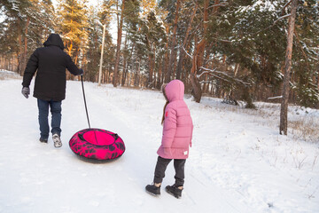 Father and daughter having fun with snow tube in the forest