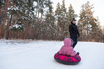 Father and daughter having fun with snow tube in the forest