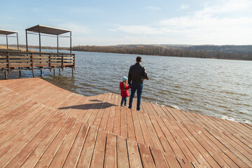 Father and daughter standing at the pier near the lake in sunny day.