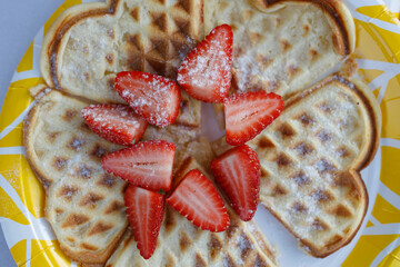 A delicious heartshaped waffle adorned with fresh strawberries placed on top, all served on a white paper plate for a delightful presentation