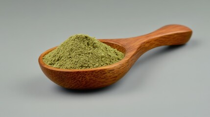 Kratom powder resting in wooden spoon on gray background