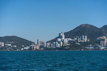Hong Kong cityscape with residential areas and green hills, taken from the water on a sunny day
