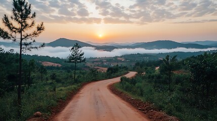 Winding dirt road through a misty mountain landscape at sunrise.