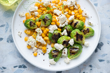 Roasted Brussels sprouts with sweet corn and cottage cheese served on a white plate, horizontal shot, middle closeup