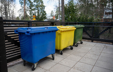 Three colored garbage bins for waste separation placed on outdoor pavement