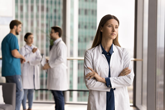 Pensive young woman doctor private medical center ceo modern hospital team leader stand by window wall lost in thoughts visualize medical business future consider healthcare innovations. Copy space - Powered by Adobe