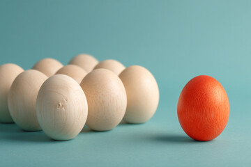 Group of beige wooden eggs and single orange egg on teal background, showcasing uniqueness and standing out from the crowd