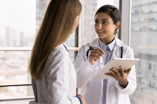 Problem solving together. Young woman doctor medical worker talk to female colleague pharmacist physician discuss healthcare research article on tablet computer screen ask opinion professional advice