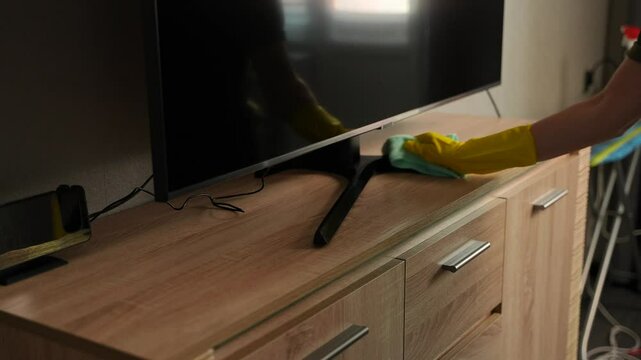 A young woman is wiping dust with a damp cloth. Cleaning the apartment from dust. Maintaining cleanliness and order in the house.