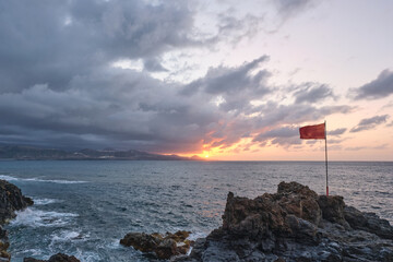 Golden hour view of a stunning sunset over the Atlantic Ocean, captured from the volcanic rocky shore of Las Canteras Beach in Las Palmas de Gran Canaria, Canary Islands. The silhouette of distant mou