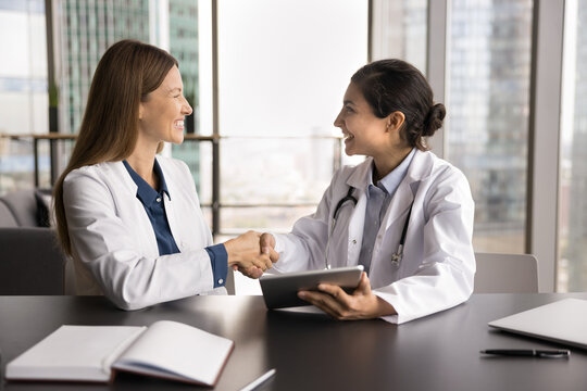 Partnership in patient care. Two happy smiling diverse women medical professionals doctor and pharmaceutical representative handshake after making deal celebrate successful cooperation in healthcare
