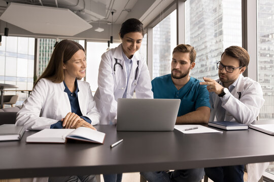 Networking and collaboration in medicine. Enthusiastic professional polyethnic doctors team hold conversation looking at notebook screen discuss patient case treatment protocol make diagnosis together