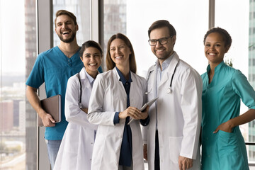 Collaboration in healthcare. Candid laughing multiethnic doctors team stand at clinic corridor having fun celebrate successful teamwork result together feel joyful inspired motivated with profession
