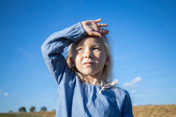 Girl child in a dress against the blue sky on a sunny day