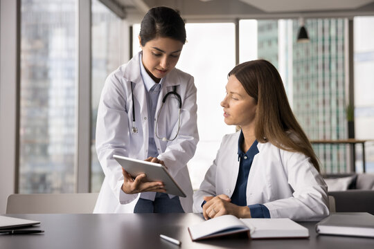 Guidance in medical training. Focused young female medic worker intern get professional advice consultation from experienced colleague mentor learn to read laboratory results looking on tablet screen