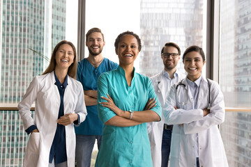 Contemporary standards in healthcare. Young modern day doctors international hospital medical workers pose for portrait together with young lady surgeon team leader in clinic office with window walls