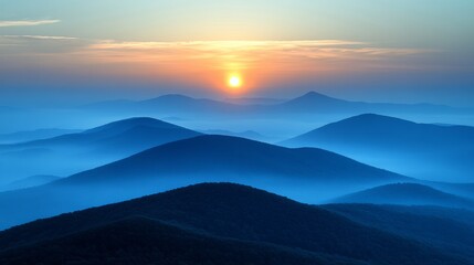 Obraz premium Sunrise over misty mountain ranges with layers of blue haze creating a serene and tranquil scene.