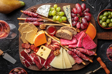 Antipasti or tapas. Charcuterie and cheese board with wine, overhead flat lay shot on a black slate background. Mediterranean food and drinks