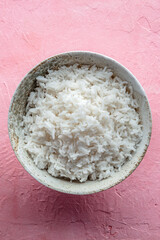 White rice, cooked. A bowl of boiled long grain rice, a simple side dish, on a pink background