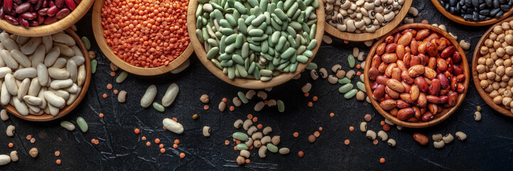 Various legumes, overhead flat lay panorama on a black background. Many different pulses, an...