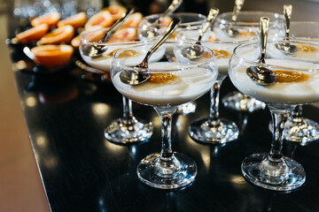 A beautifully arranged row of elegant wine glasses, each filled with a delightful dessert, accompanied by spoons placed neatly on a table