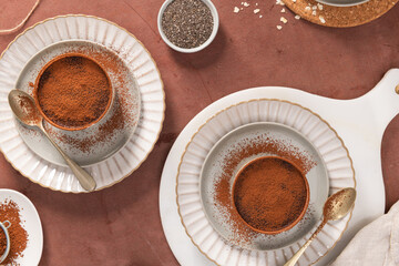 Two Chocolate desserts with a dusting of cocoa powder on white plates, accompanied by gold spoons, set on a brown surface with a white cloth in the background. Top view