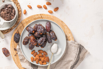 Healthy snack ingredients including medjool dates, almonds, shredded coconut, and dark chocolate chunks arranged on a wooden board and a white plate. Top view