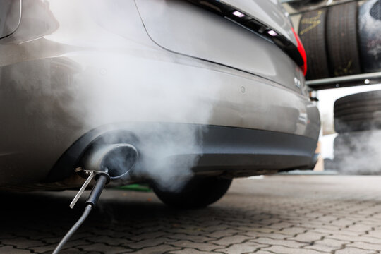 Car exhaust pipe emits dense smoke during emission test on city pavement. Pollution control device measures harmful gases. Service car center garage workshop.  Automobile repair check up diagnosis