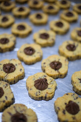 Close-up of flower-shaped chocolate chip cookies with a dollop of chocolate filling in the center, arranged on a baking tray. The cookies have a golden-brown texture with a decorative pattern.