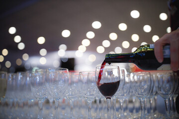 A person is skillfully pouring a rich, deep red wine into a glass, creating an enticing visual of liquid being transferred elegantly