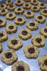 Close-up of flower-shaped chocolate chip cookies with a dollop of chocolate filling in the center, arranged on a baking tray. The cookies have a golden-brown texture with a decorative pattern.