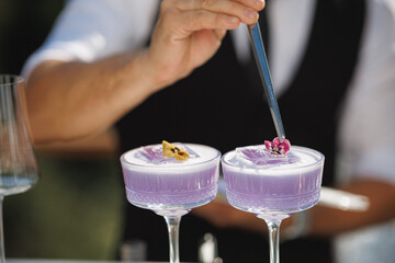 A bartender is carefully stirring two vibrant purple cocktails using a long spoon, creating a delightful blend of flavors within them