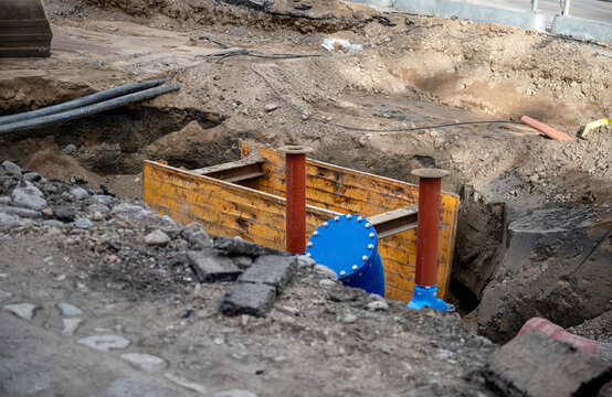 Underground pipeline construction site with trench shoring and blue valve exposed