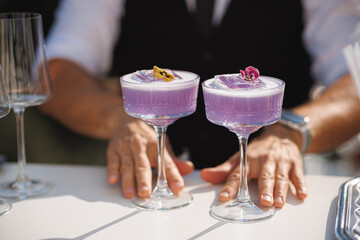 A skilled bartender is meticulously preparing two vibrant purple cocktails on a beautifully...