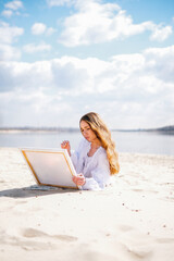 Cute teenage girl painting a picture on the river bank on a sunny day