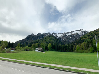 A scenic view of mountains with snow on the peaks, surrounded by green meadows and trees, with a house in the foreground.