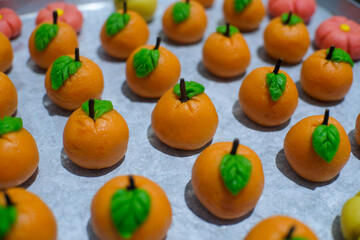 Close-up of beautifully crafted *nastar*, Indonesian pineapple tarts, shaped like miniature oranges with green leaves and tiny stems, arranged on a baking tray. 