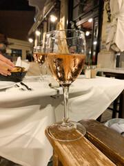Glass of rosé wine on a wooden armrest at a cozy outdoor restaurant at night.
