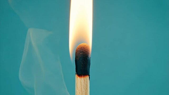 Lit matchstick in close-up, teal background