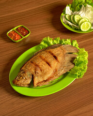 Crispy Fried Gourami Fish Served with Fresh Vegetables and Spicy Sambal on the Side, A Delicious Traditional Indonesian Culinary Experience.