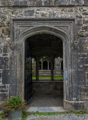 An arched stone doorway with intricate carvings leading to a cloister, partially obscured by a...