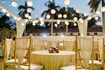 Elegant outdoor event with paper lanterns, gold table settings, and flower centerpieces. Festive and romantic ambiance for celebrations.