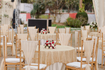 Elegant outdoor wedding reception with gold tablecloths, floral centerpieces, and stylish chair decor in a sophisticated setting.