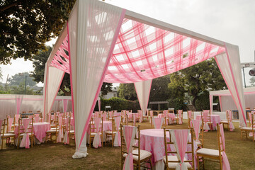 Outdoor celebration setting with a decorated tent and pink accents on tables and chairs, creating a festive atmosphere.