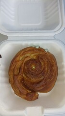 Freshly Baked Pastry in a Takeout Box. A close-up of a golden-brown pastry with a swirl pattern, placed inside a white takeout box, showcasing its delicious texture